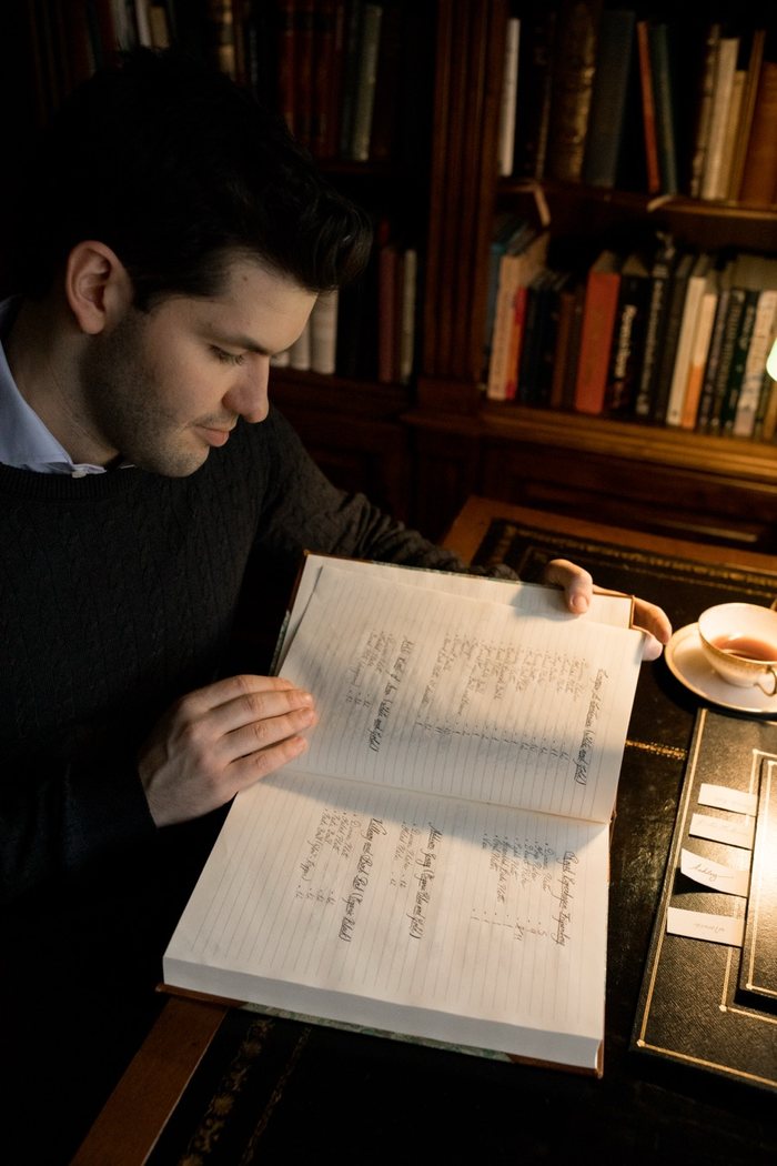 Rafa de Campos Salles folheia um caderno manuscrito numa biblioteca, com uma xícara de chá sobre a mesa.