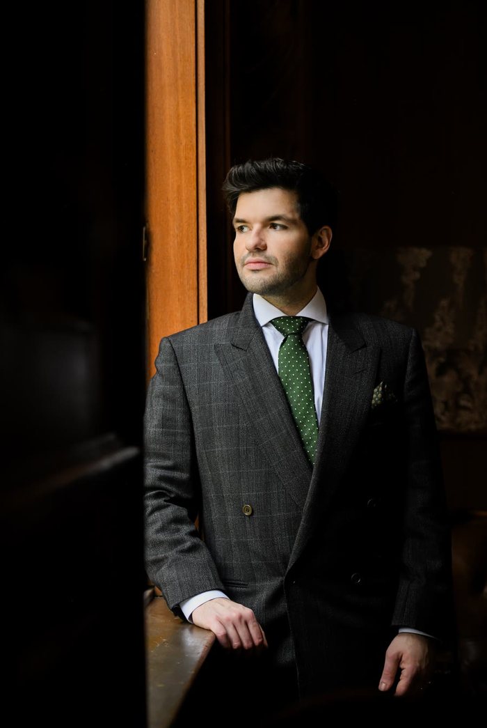 Rafa de Campos Salles, de terno cinza trespassado e gravata verde, junto a uma janela.