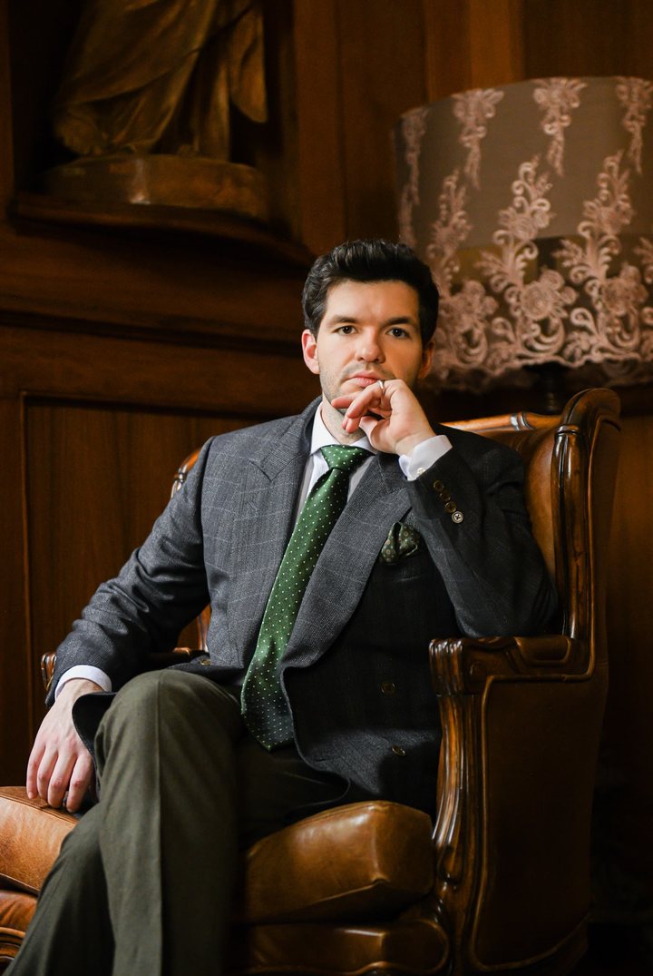 Rafa de Campos Salles, de terno cinza e gravata verde, sentado numa poltrona de couro em uma sala com painéis de madeira.